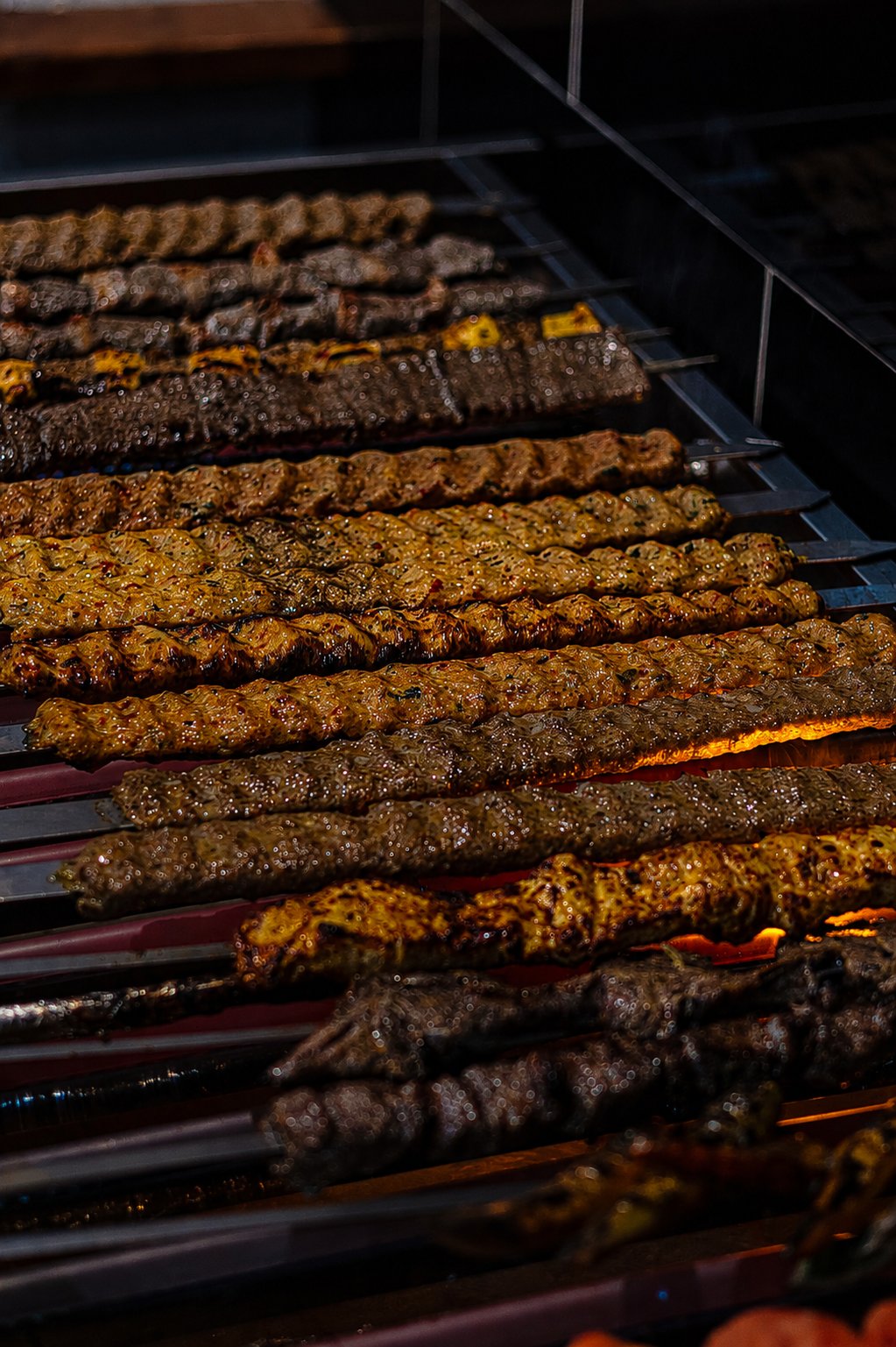 Rows of hand-pressed koobideh skewers cooking over the open flame grill at Reyhan in Weston ACT